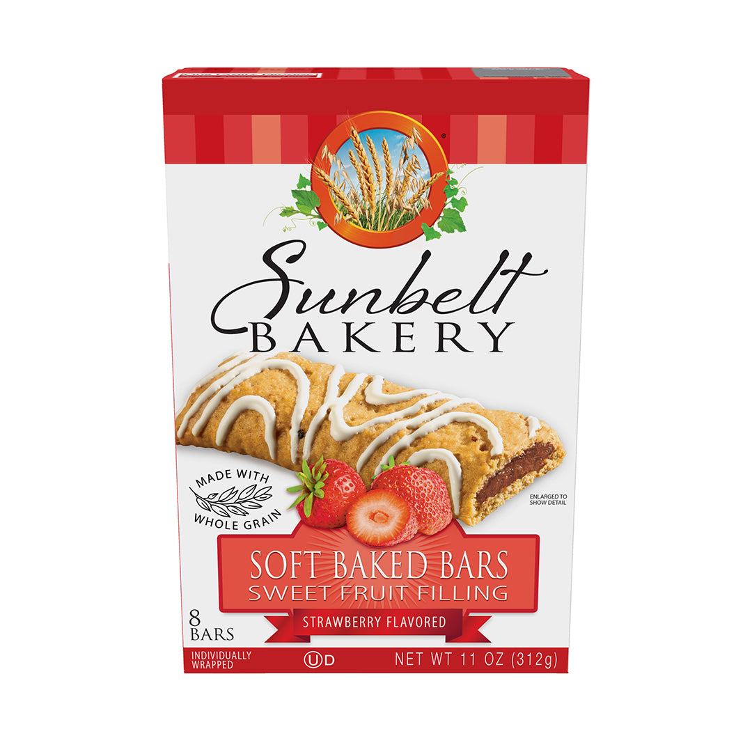 Box of Sunbelt Bakery Strawberry Flavored Soft Baked Bars with the image of a bar topped with white glaze and a strawberry-flavored jam center. Below the bar, fresh strawberry slices accent the product visually. The packaging indicates 'Made with Whole Grain' and '8 Individually Wrapped Bars', with a net weight of 11 oz (312g). The box has a red gingham pattern along the top, and the Sunbelt Bakery brand logo with wheat imagery is at the top center.